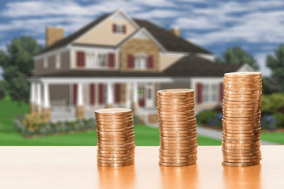 Three ascending stacks of coins on a wooden surface with a blurred image of a large two-story house in the background, symbolizing infinite banking for real estate investors.