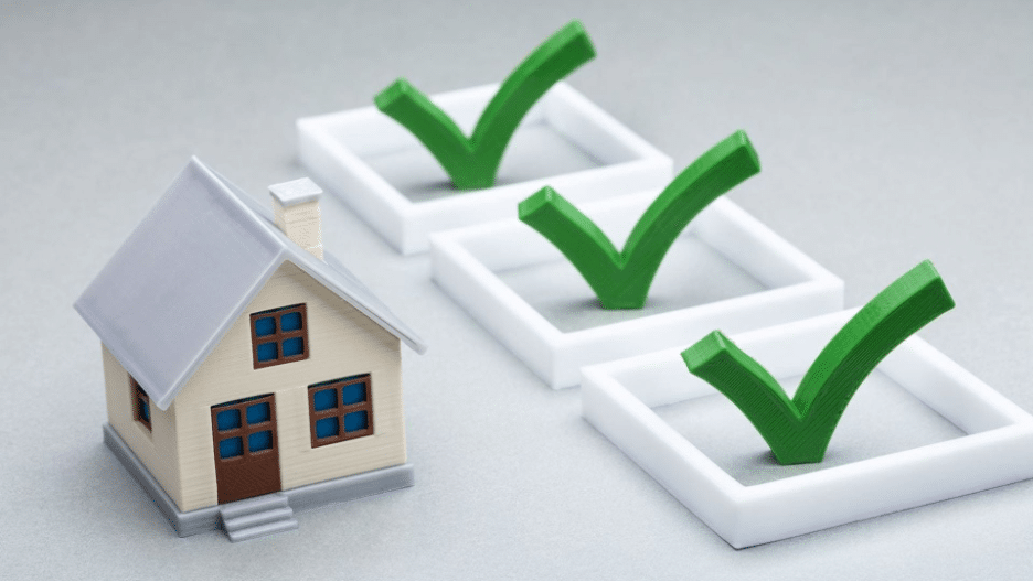 A miniature house model with three green check marks in check boxes lined up beside it, representing the completion of steps or preparation tips in a home buying checklist.