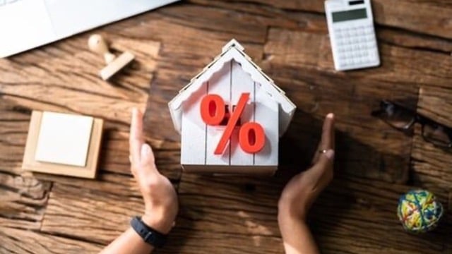 Hands framing a model house with a red percentage sign, highlighting interest rates or financial aspects of property management.