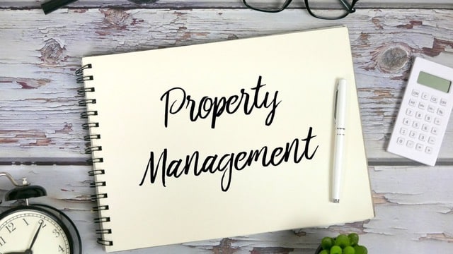 Notebook with 'Property Management' written on it, alongside a calculator and glasses, representing self-management vs property management company decisions.