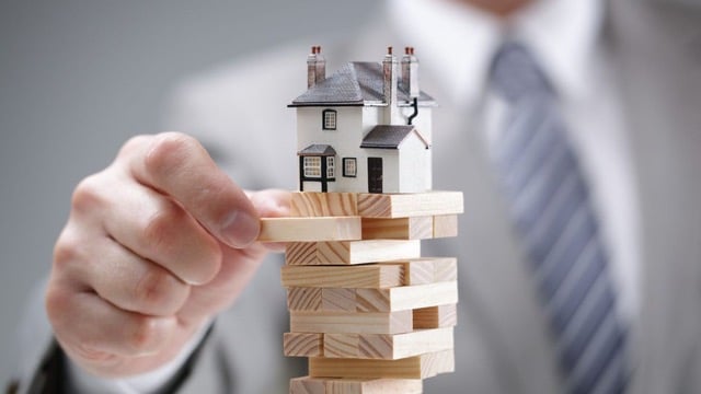 Businessperson strategically placing the final piece on a Jenga game with a miniature house on top, representing common mistakes new real estate investors should avoid