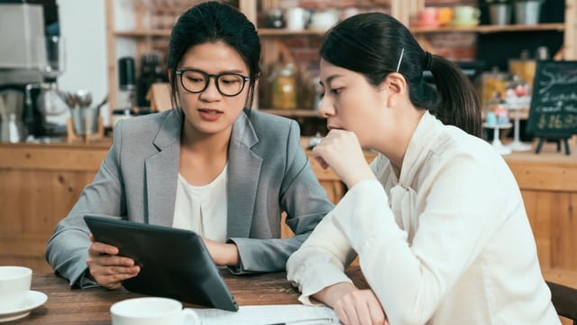 Two professionals discussing strategies on a tablet in a cafe, exemplifying effective communication with real estate investors after funding.