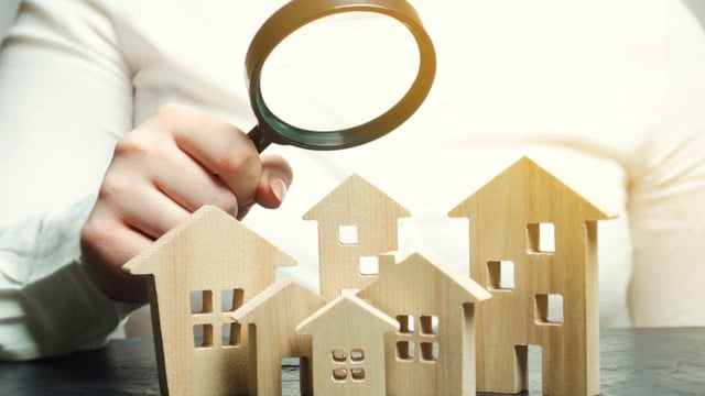 Person examining wooden house models with a magnifying glass, representing due diligence in a Private Lending Checklist for Real Estate