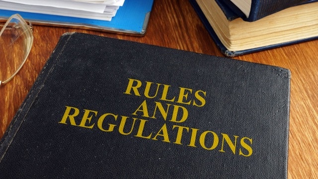 Black book with 'RULES AND REGULATIONS' title on a wooden desk, indicating the importance of legal guidelines in how to raise rent without losing tenants