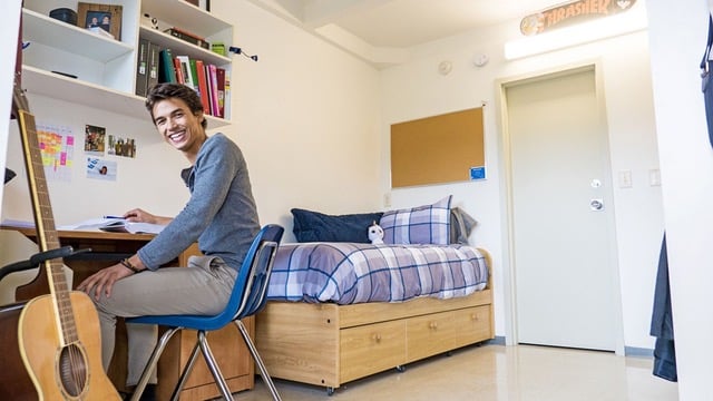 Smiling university student in a well-organized dorm room, representing a smart student housing investment opportunity.