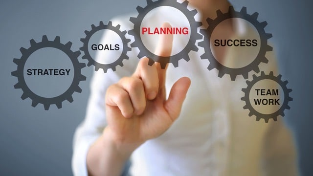A suitable alt text for this image could be: "A professional touching a virtual interface with interconnected gears labeled 'STRATEGY', 'GOALS', 'PLANNING', 'SUCCESS', and 'TEAM WORK'