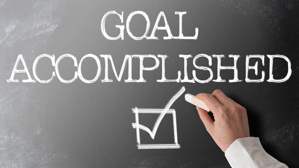 "Goal Accomplished" written on a chalkboard, with a hand drawing a checkmark in a box, symbolizing the successful completion of a real estate exit strategy.