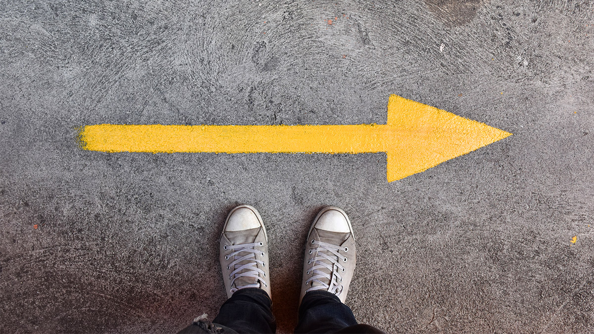 Yellow arrow pointing forward on a concrete surface with a person standing at the starting point, symbolizing direction for a real estate exit strategy.