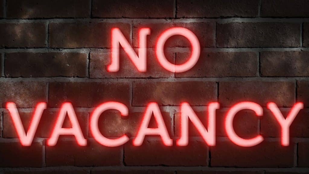 A glowing red neon sign reading "No Vacancy" against a brick wall, symbolizing challenges facing short-term rentals in Canada due to new regulations.