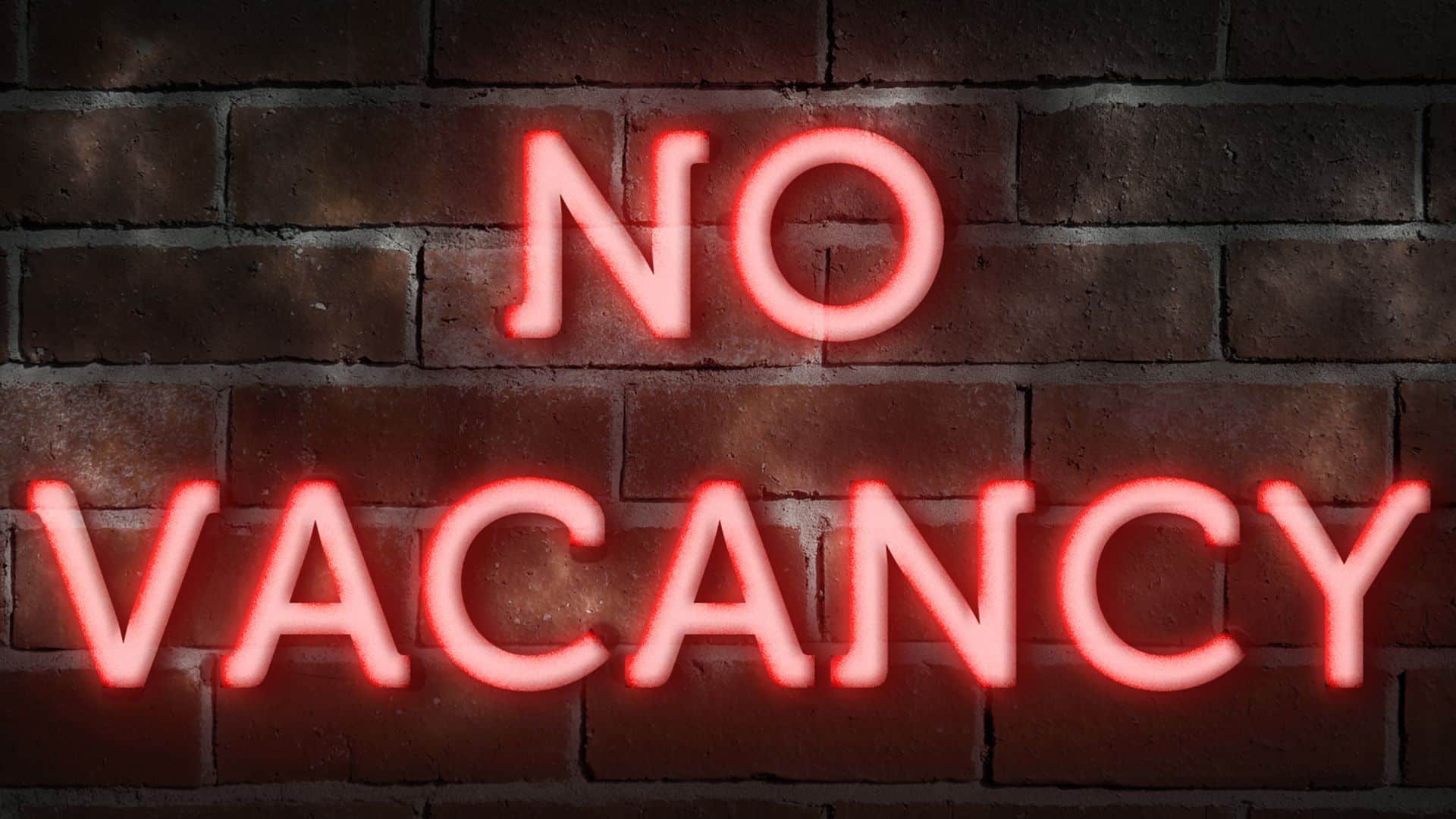 A glowing red neon sign reading "No Vacancy" against a brick wall, symbolizing challenges facing short-term rentals in Canada due to new regulations.