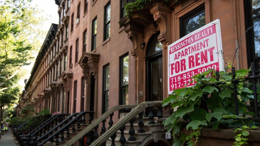 A "For Rent" sign in front of a brownstone representing the demand and opportunities in multifamily investment.