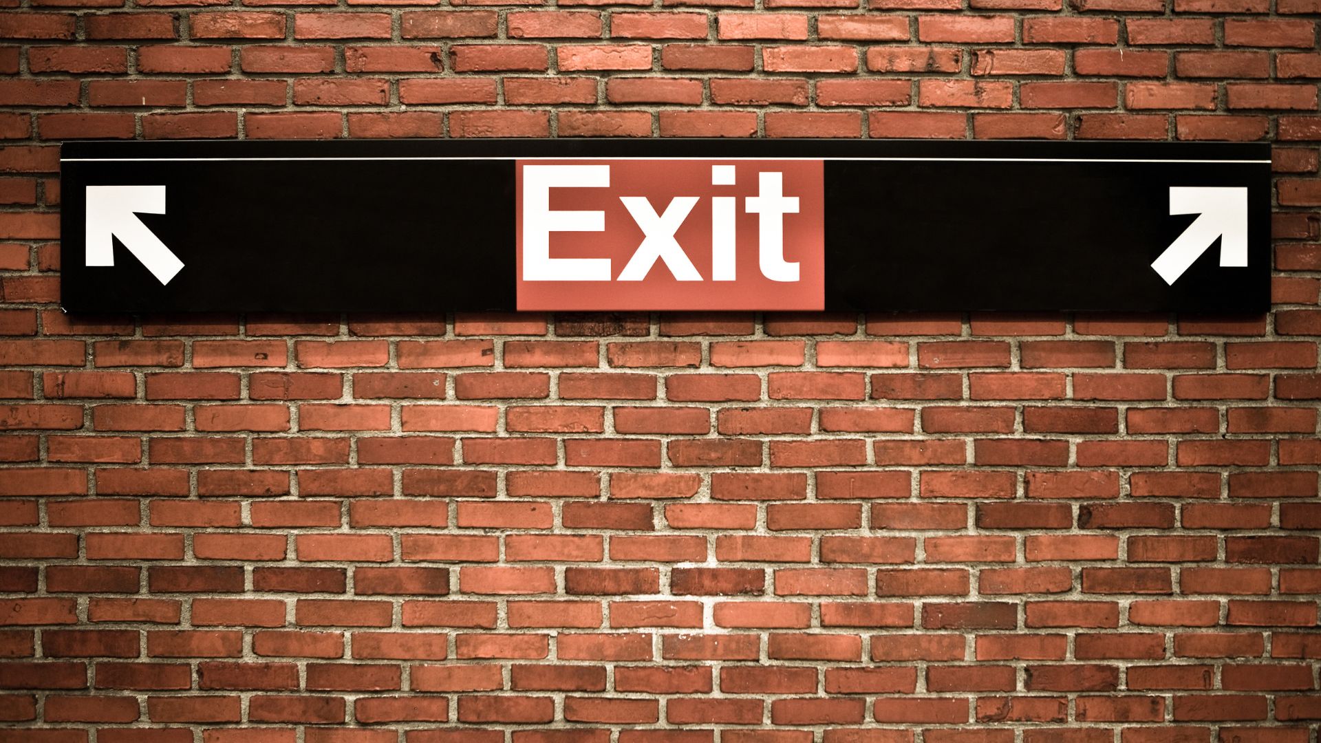 A black and red "Exit" sign on a brick wall, symbolizing the importance of knowing when to walk away from a real estate deal.