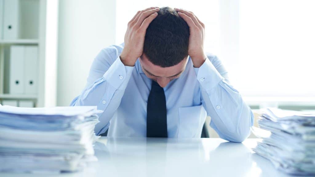 A stressed businessman at a desk with stacks of paperwork, symbolizing the need for a real estate tax strategy during tax season.