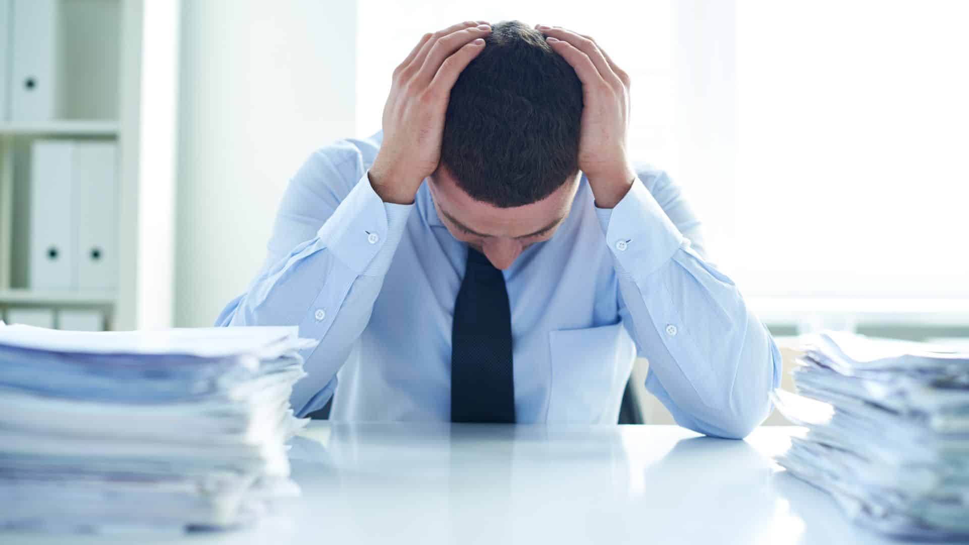 A stressed businessman at a desk with stacks of paperwork, symbolizing the need for a real estate tax strategy during tax season.